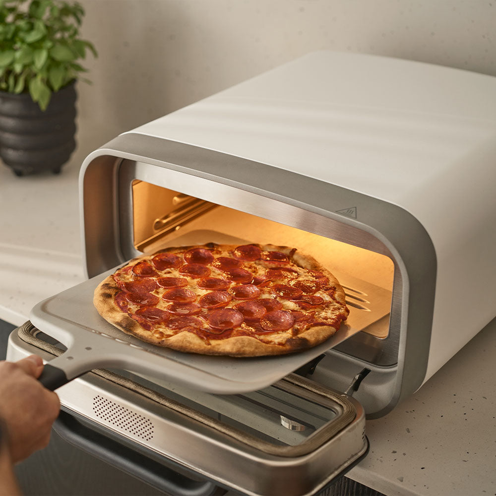 A hand launching a pepperoni pizza into the Volt 2 oven
