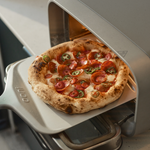 Pizza with pepperoni and jalapeños being taken out of the Volt 2 Electric Pizza Oven.