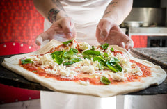 a pair of hands preparing a marghertia pizza