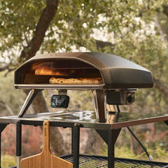 The Ooni Koda 2 Pro pizza oven on a metal table with a blurred garden background