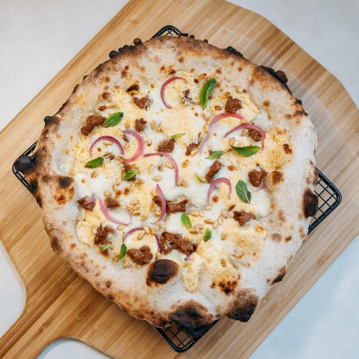 apricot, feta, merguez sausage, and pickled onion pizza on a bamboo peel