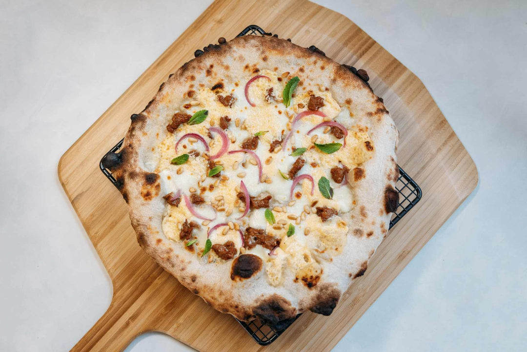 apricot, feta, merguez sausage, and pickled onion pizza on a bamboo peel