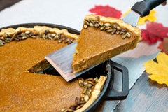 Candied pumpkin seed pumpkin pie in a cast iron pan with a slice being taken out