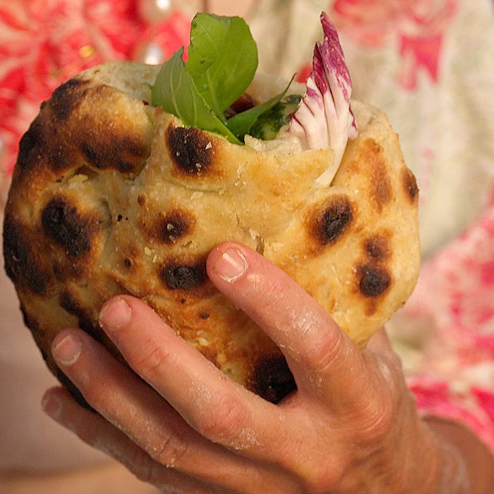 Hand holding a cooked pizzette stuffed with baby peppers, mozzarella, radicchio and basil.