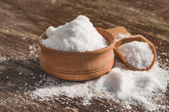 Wooden bowl of salt next to a large wooden spoon with salt.