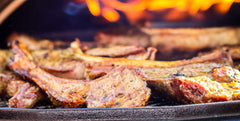 Lamb chops on a cast iron pan being grilled in an Ooni Karu 16 pizza oven