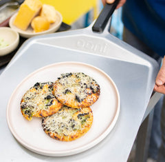 Potato flatbreads covered with garlic butter, cheese and kale on a steel pizza peel