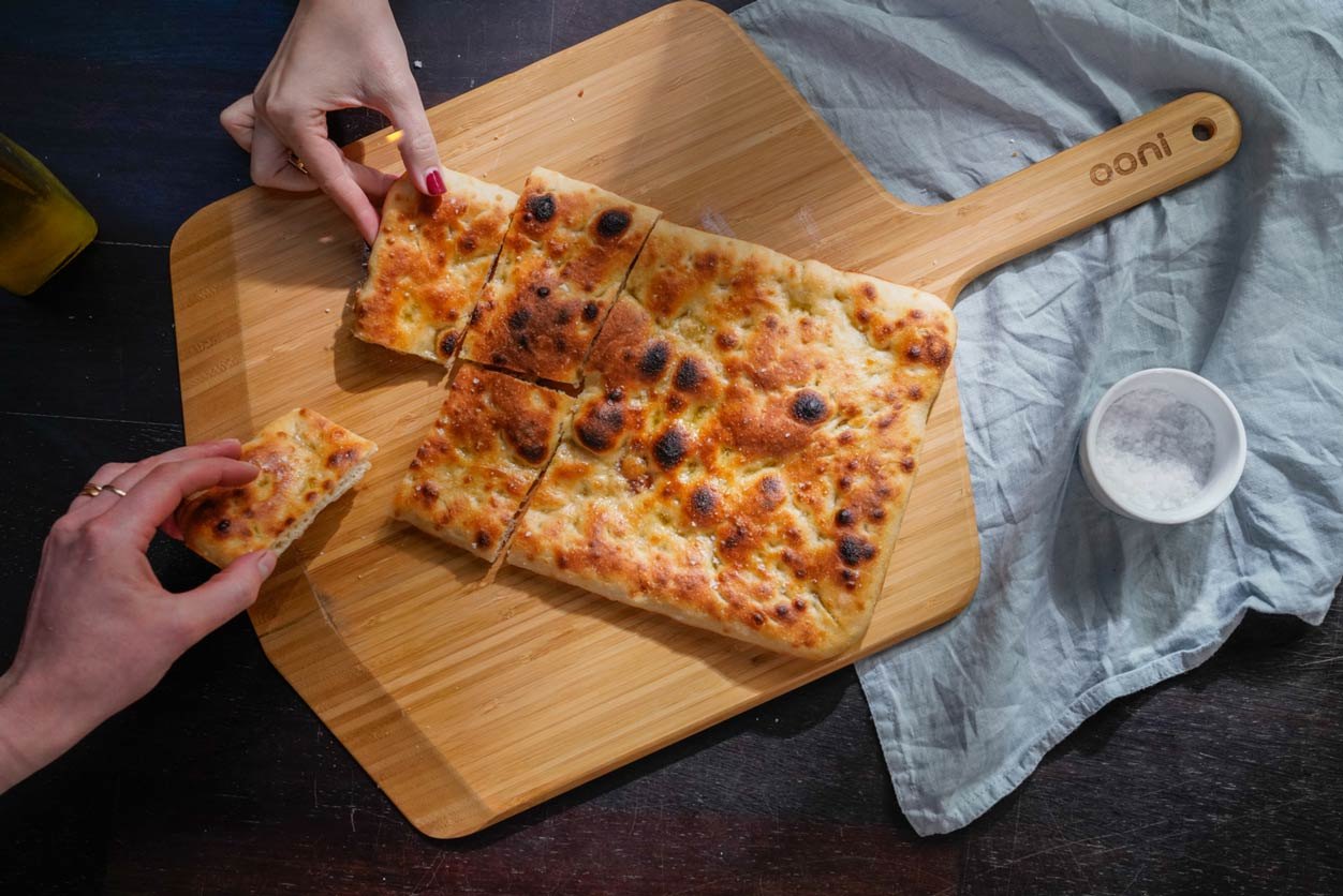 wo hands holding pieces of Roman pizza on an Ooni Bamboo Pizza Peel & Serving Board.