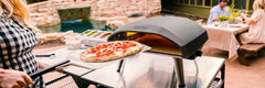 A man launches a pizza into the Koda 16 pizza oven using a perforated pizza peel