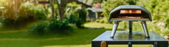 The Koda 12 pizza oven on a metal table with a blurred garden back drop