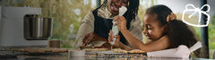 A mother and daughter icing cookies in a modern kitchen setting with an Ooni Halo Pro Spiral Mixer in the background.