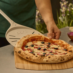Person sliding a cooked pizza onto a wooden board using an Ooni turning peel.