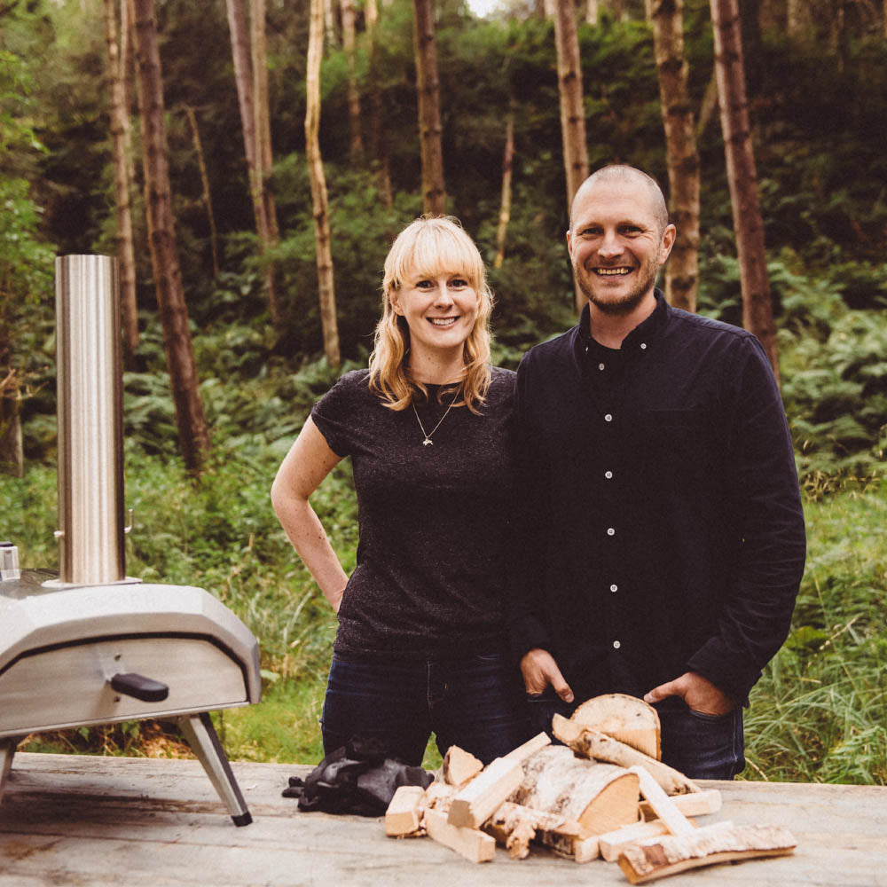Founders of Ooni, Kristian Tapaninaho and Darina Garland, stand beside a table with the Karu 12 oven 
