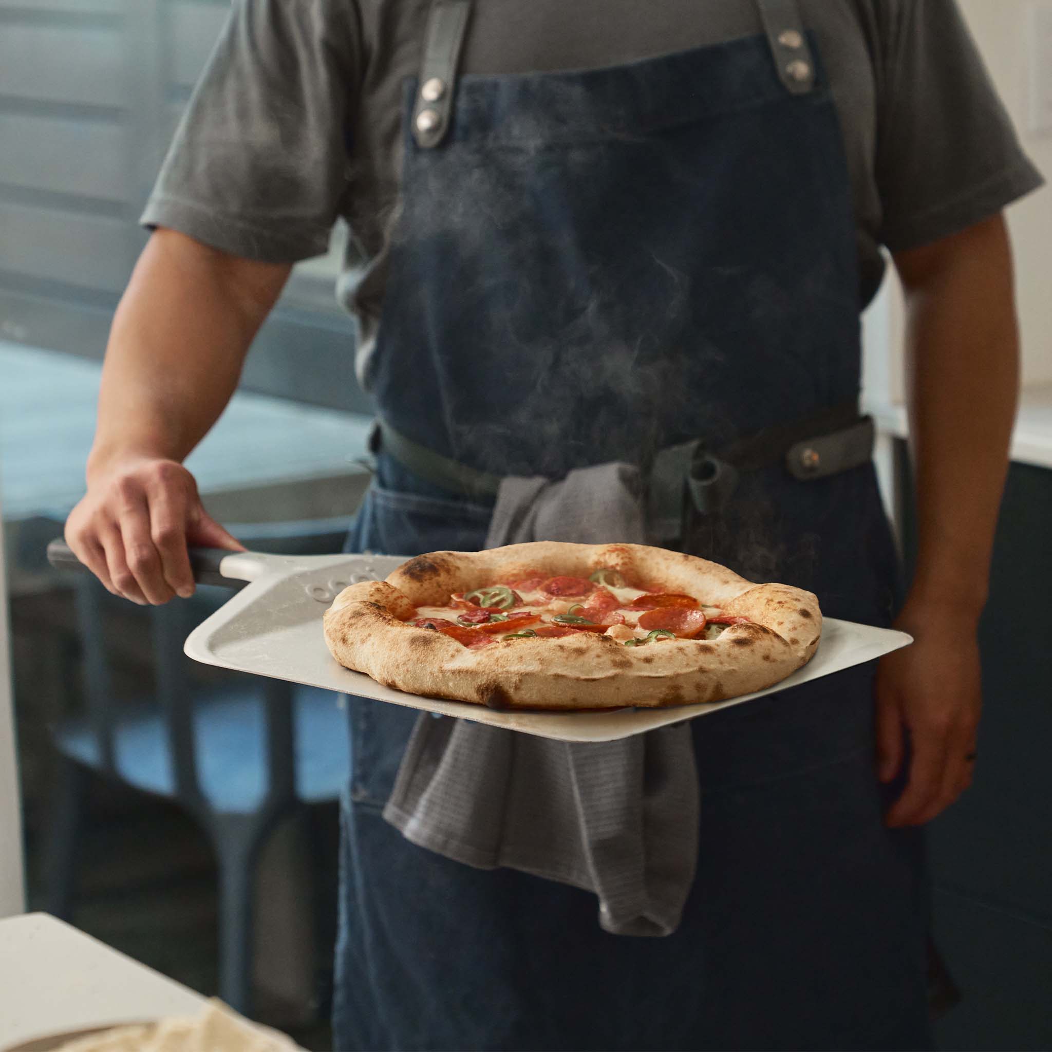 Man holding a Ooni Compact pizza peel with a fresh neapolitan pizza on top.