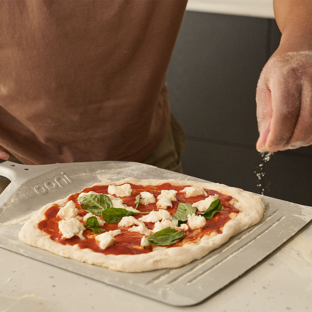 Sprinkling flour on Ooni compact pizza peel with Neapolitan pizza.