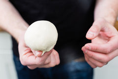 A person holding a perfectly smooth ball of Ooni pizza dough.