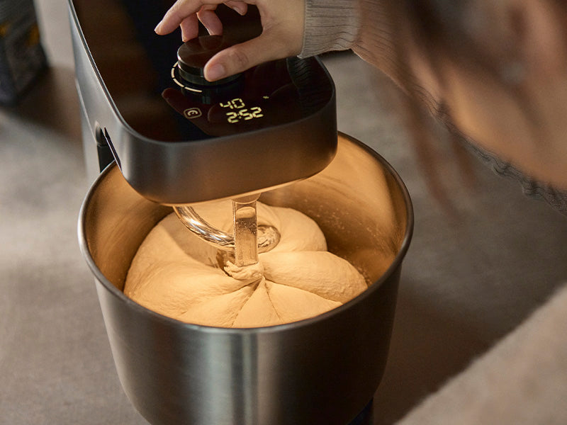 A close up of a hand moving the dial of the Halo Pro Spiral Mixer and dough being mixed in the stainless steel bowl.