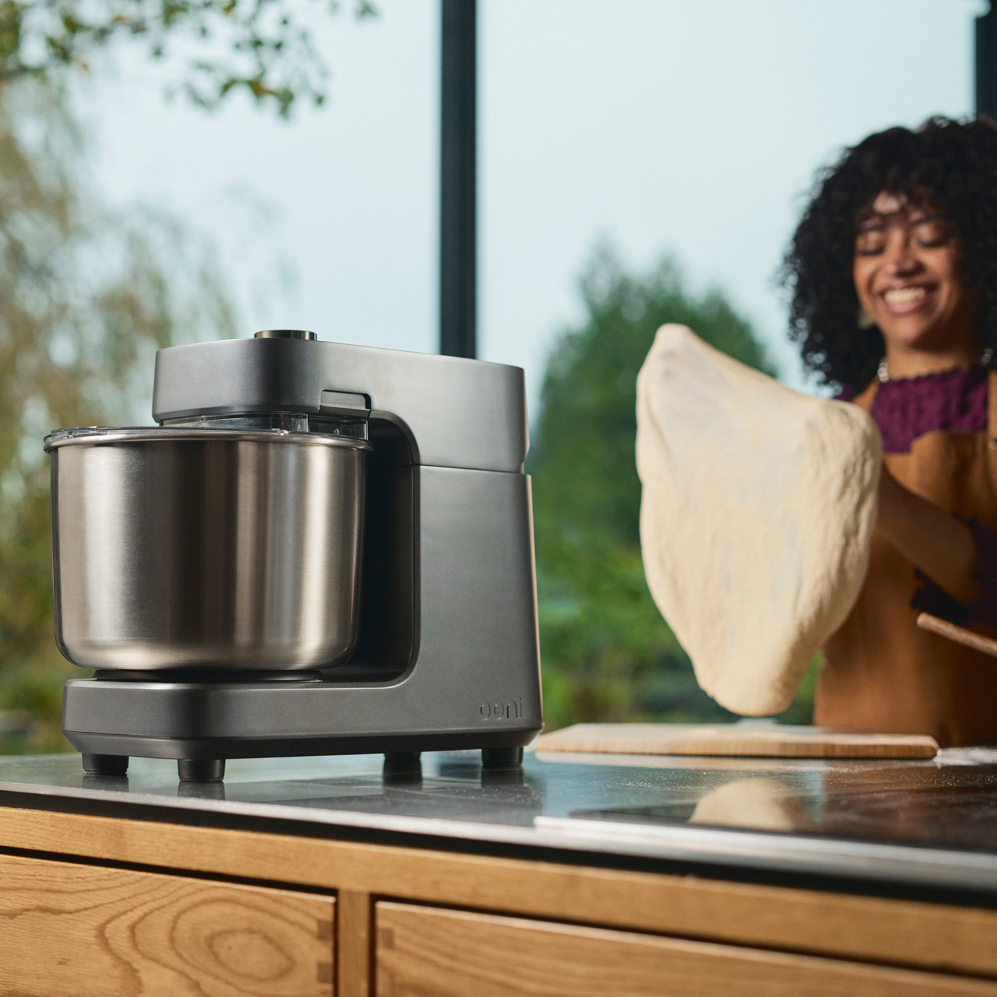 Ooni Halo Pro Spiral Mixer on a counter with a person holding pizza dough in the background