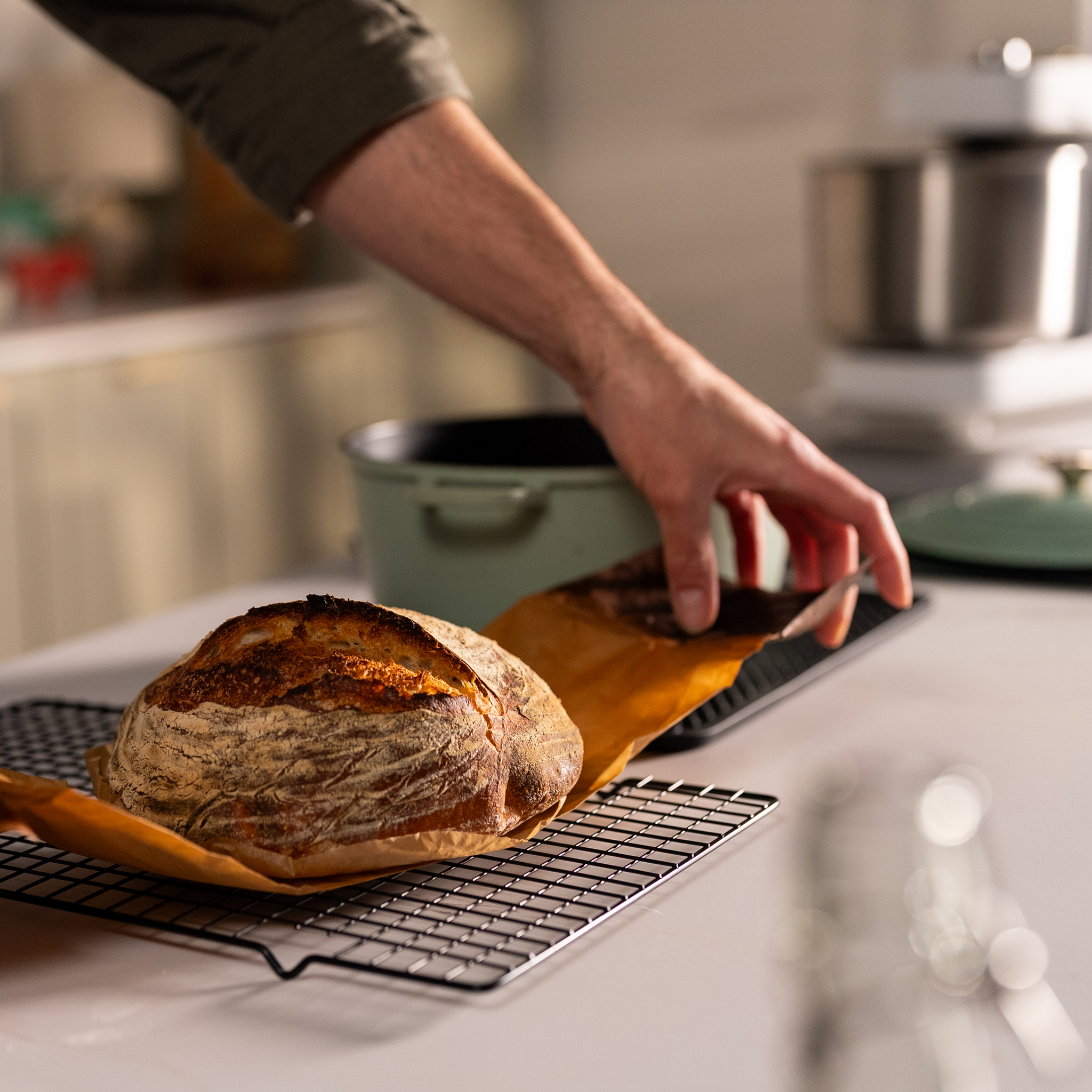 Person placing a loaf of bread on a cooling rack in a kitchen.