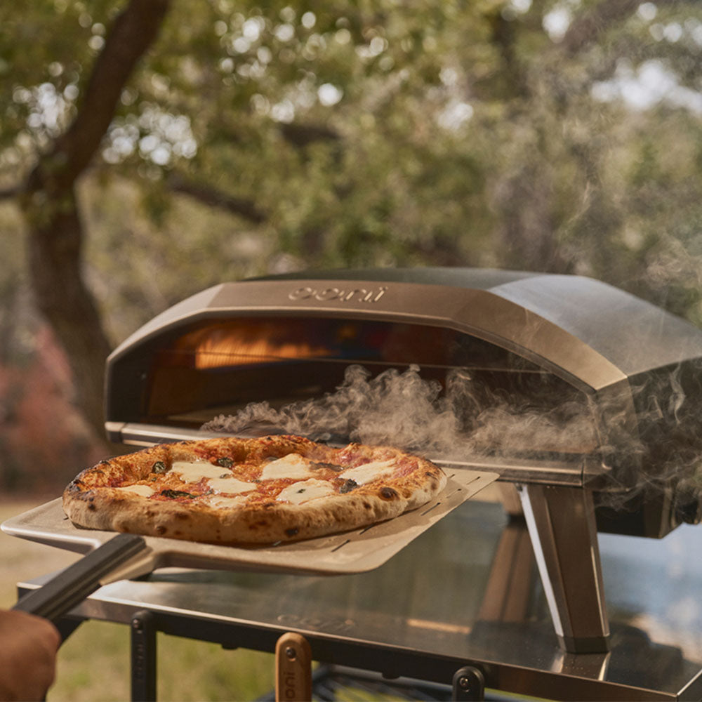 Koda 2 Pro pizza oven with a pizza being cooked, set against a natural background.