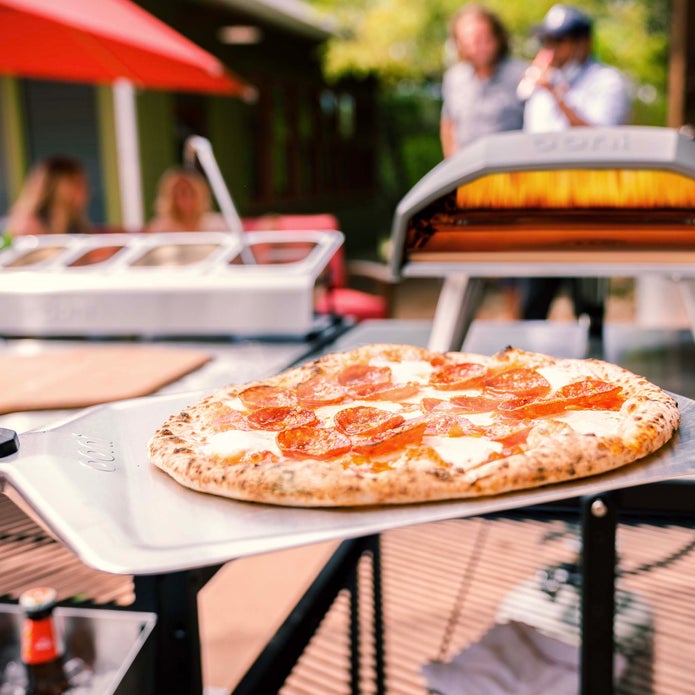 Cooked pepperoni pizza on the 12" Ooni Pizza Peel with a Koda 12 in the background