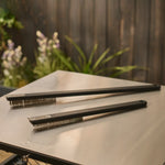 Two Ooni oven brushes on a metal table with a garden background
