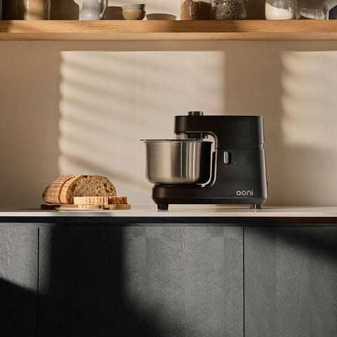The Ooni Halo Core Spiral Mixer in a modern kitchen setting with a baked load of bread beside it.