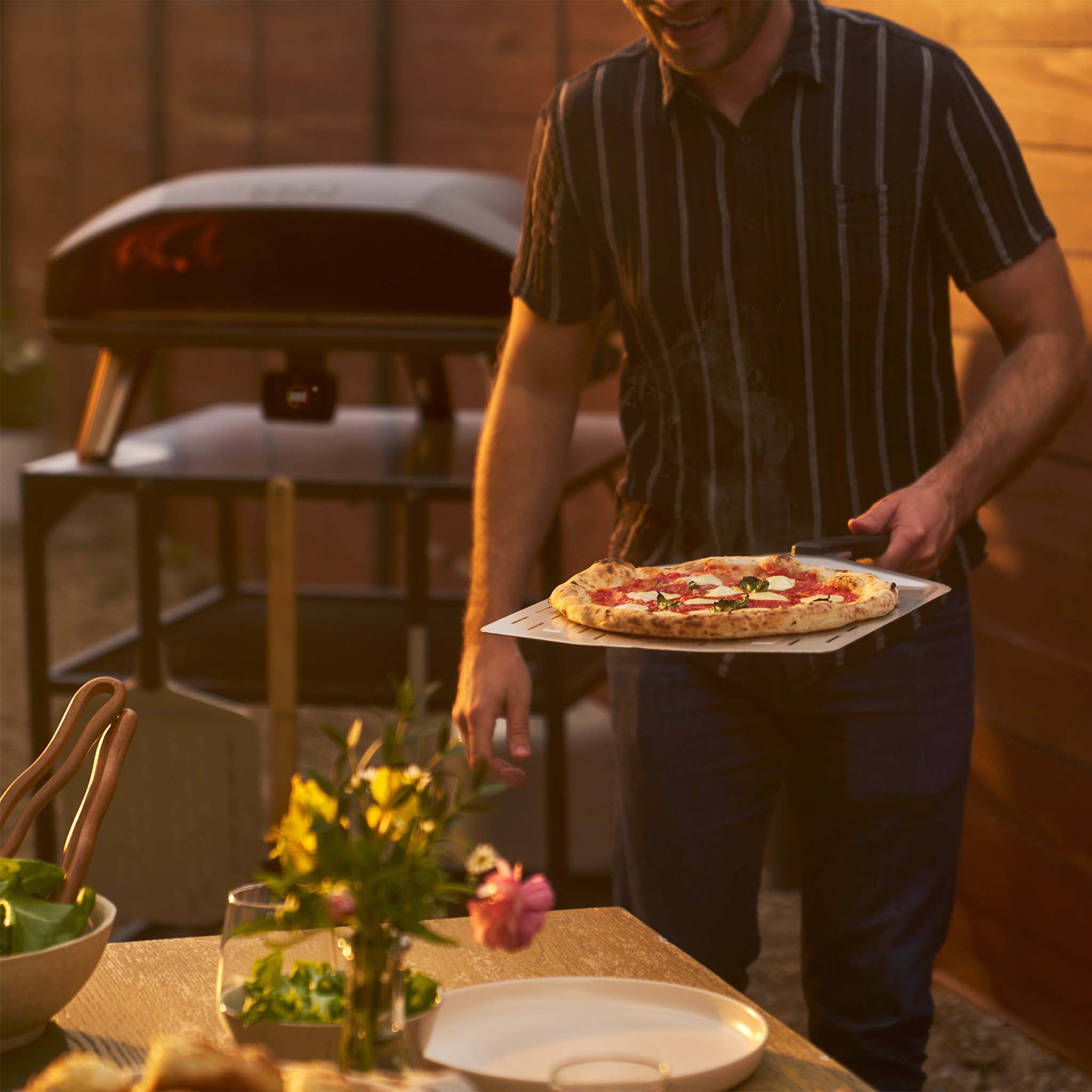Koda 2 Max in an outdoor setting with a man serving pizza on top of a perforated peel