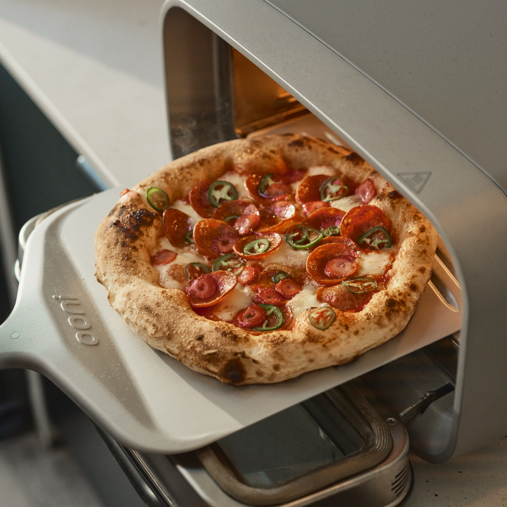 Pizza with pepperoni and jalapeños being taken out of the Ooni Volt 2 Pizza Oven.