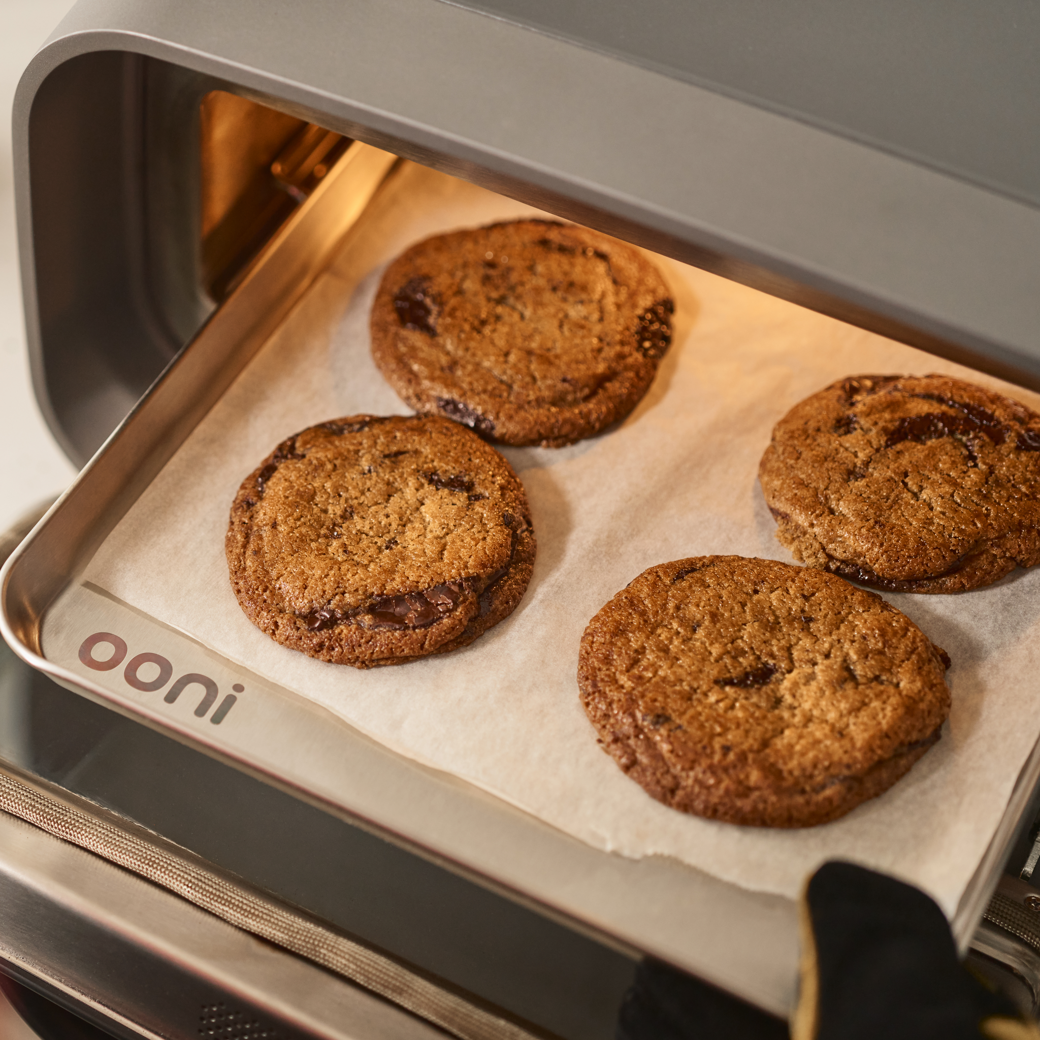 Cookies baking in the Ooni Volt 2 pizza oven with a person wearing a black glove holding the door open.