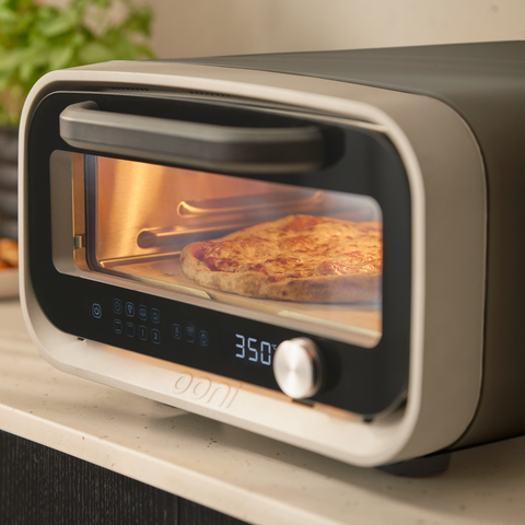 Ooni Volt 2 Polar White with a pizza inside on a kitchen counter.