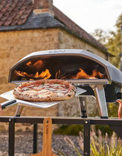 A man launches a pizza into the Koda 16 pizza oven using a perforated pizza peel