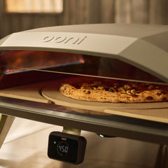 A pizza with a charred crust baking inside an Ooni oven, with the Ooni logo clearly embossed on the rotating pizza stone.